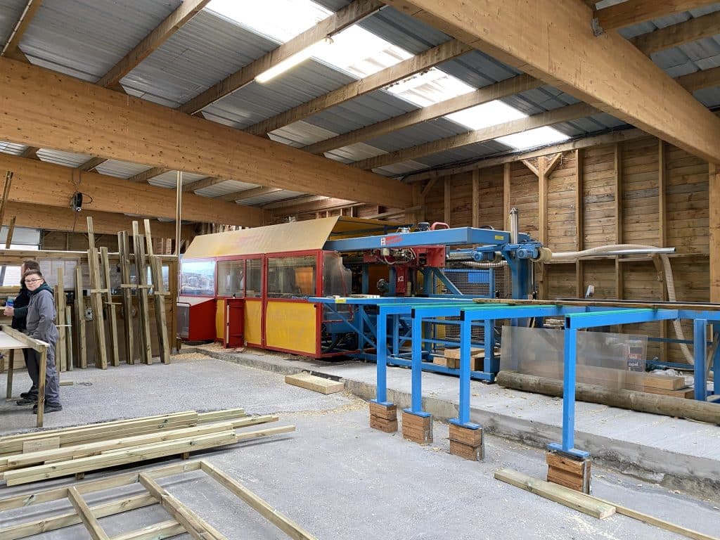 Collaboratrice de l'équipe Abri Français dans l'atelier scierie avec machine bleue et cabine rouge jaune